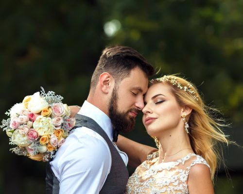 Stylish couple of happy newlyweds posing in the park on their wedding day. Perfect couple bride.